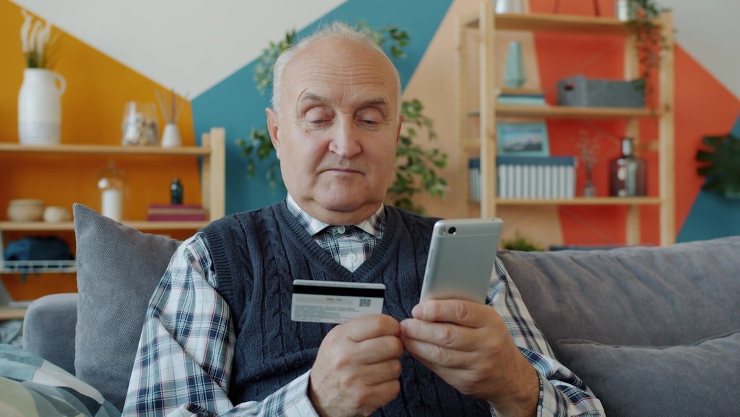 Elderly man holding credit card and smartphone for online shopping.