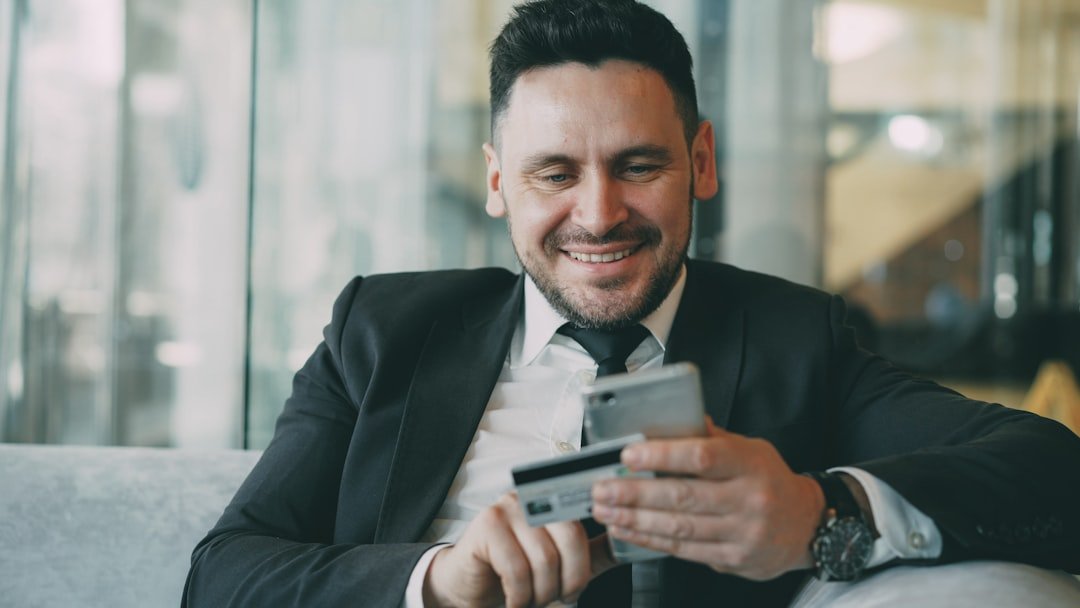 Man in suit smiling while holding phone and credit card