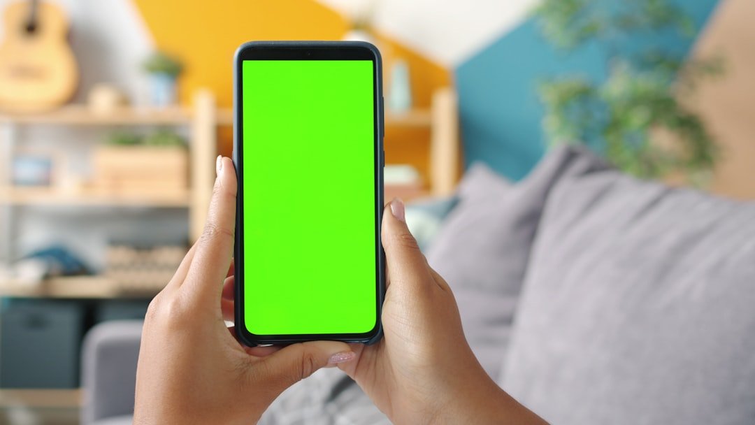 Hands holding a smartphone with a green screen.